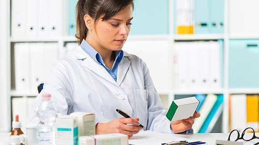 Farmacêutica faz anotações observando caixa de medicamento