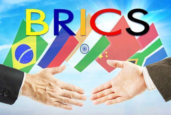 Ilustração com duas mãos se aproximando para aperto de mãos. Ao fundo bandeiras dos países e letreiro com o nome BRICS