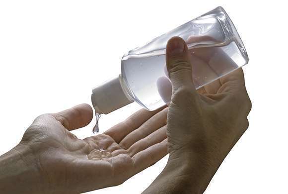 Foto mostra mãos segurando uma embalagem e aplicando álcool gel