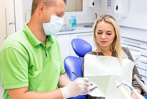 Dentista prescreve medicamento enquanto mulher aguarda sentada na cadeira de atendimento