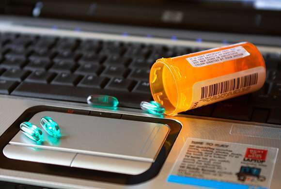 Imagem em primeiro plano de um teclado de notebook com um frasco de medicamento manipulado sobre o mouse